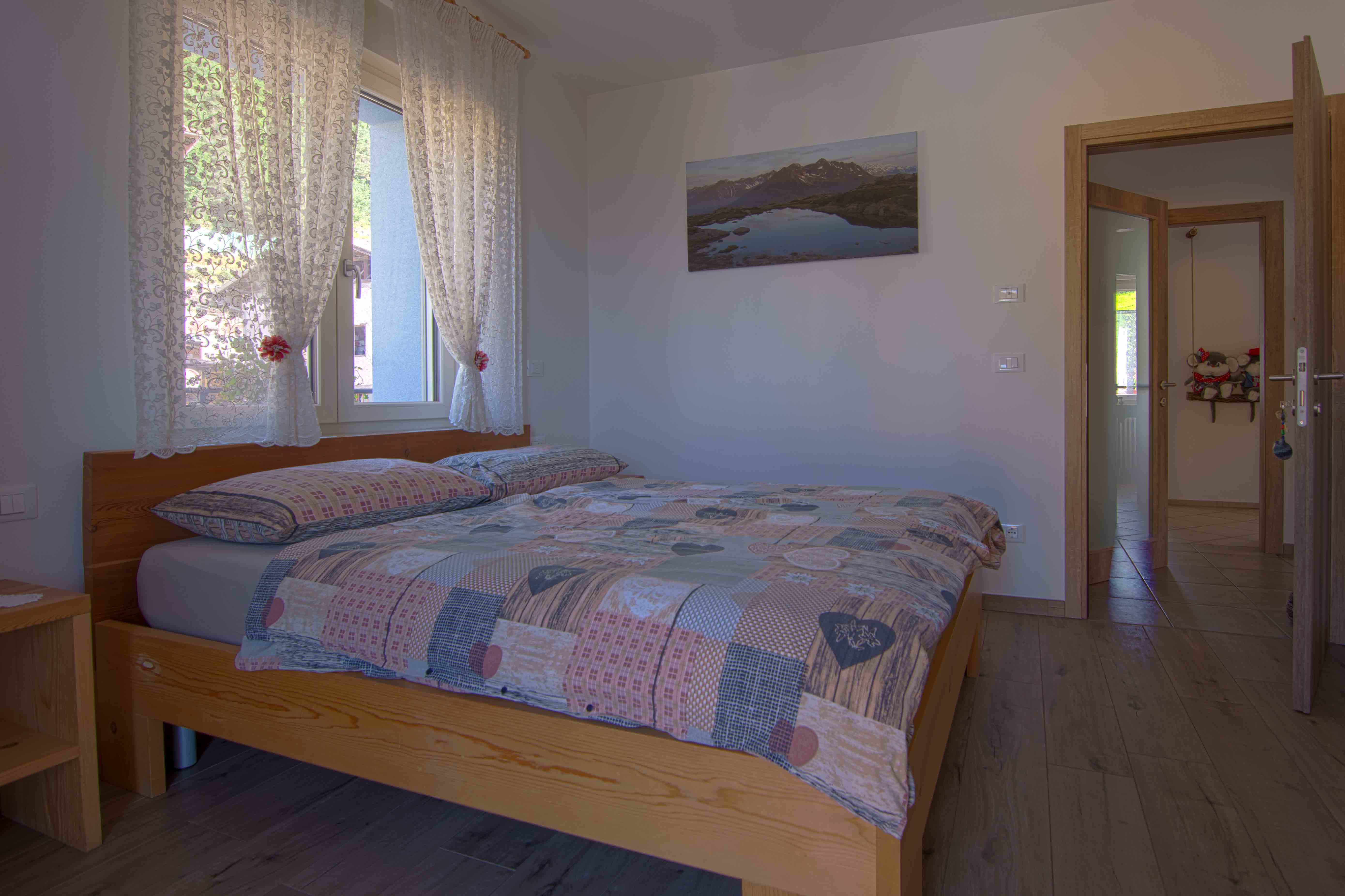 Camera Larix. Seconda prospettiva della camera matrimoniale spaziosa con decorazioni raffinate in legno con paesaggi di montagna tipici del Trentino.
