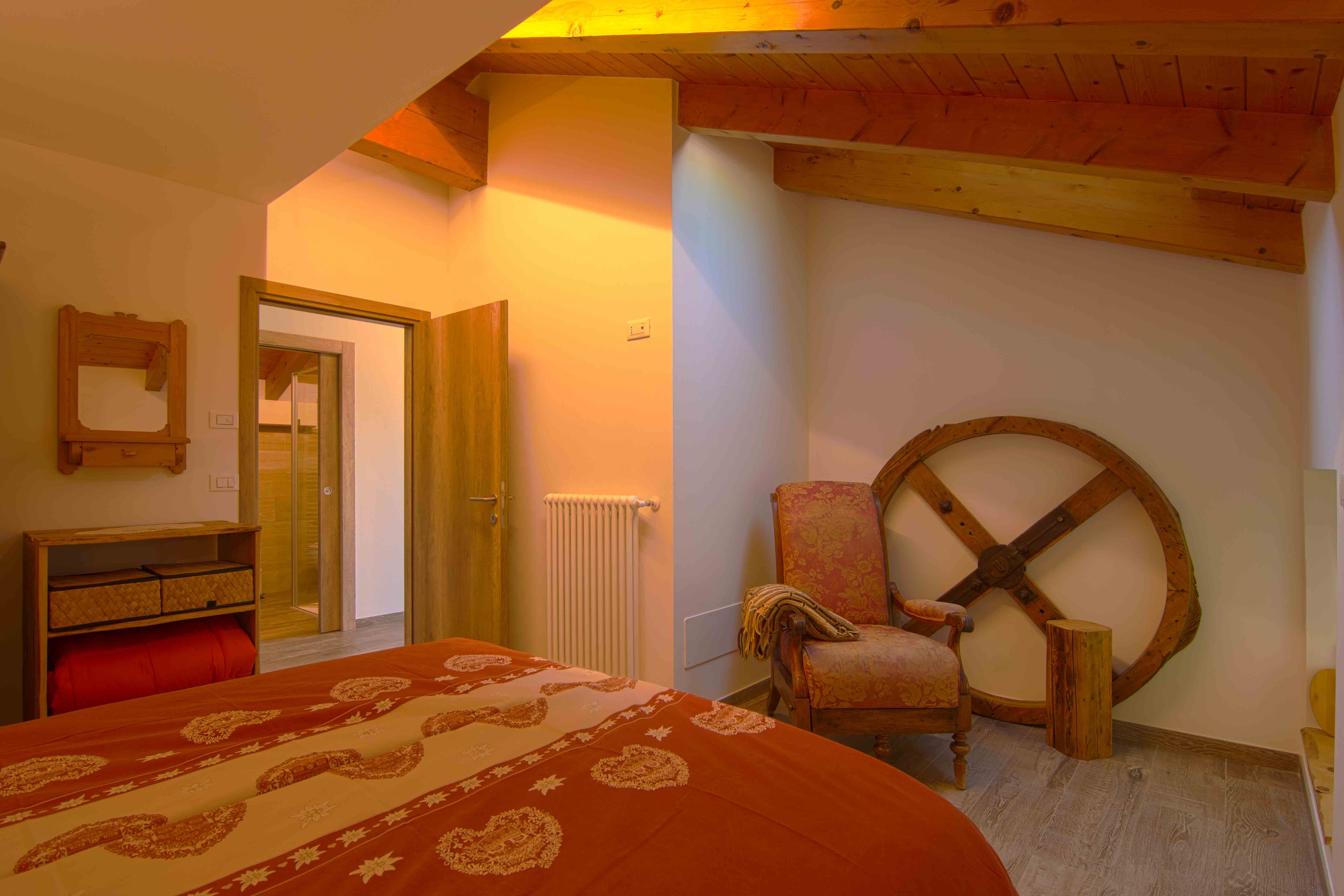 Camera Sorasu. Camera da letto matrimoniale con elegante poltrona e decorazioni in legno.