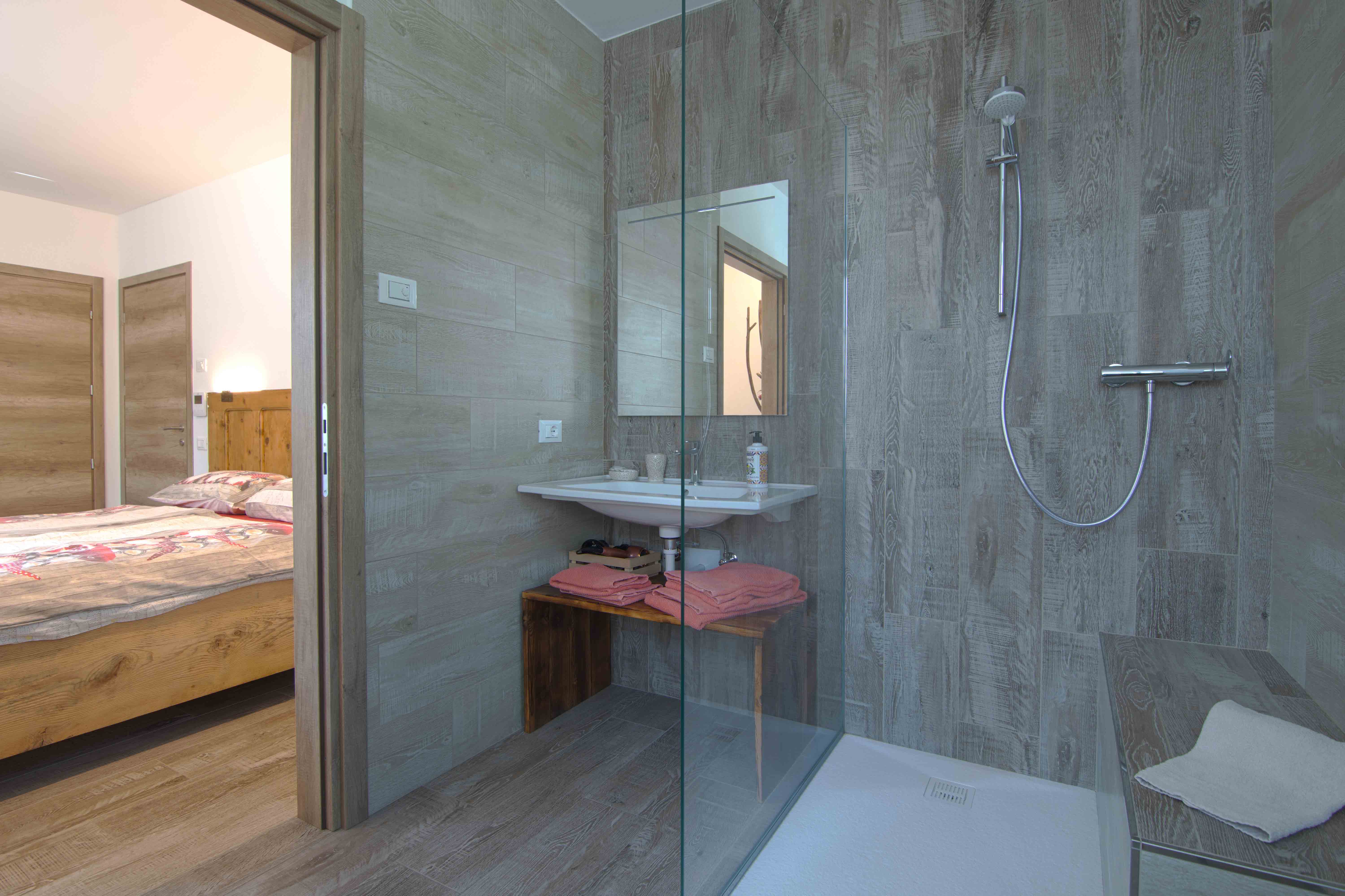 Camera Sous. Secondo bagno con doccia e decorazioni in legno.